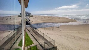 A beach view from a building with a glass facade, a sandy beach, and a rocky outcrop in the distance.