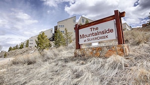 Une enseigne pour « The Mountainside at Silvercreek », avec un socle en pierre et un cadre en bois, placée sur un fond composé d’immeubles résidentiels et d’herbe sèche.