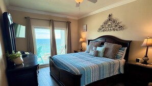 Een slaapkamer met een bed, een plafondventilator, een nachtkastje, een dressoir, een televisie en uitzicht op de oceaan.