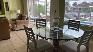 A dining area with a glass table and chairs, a sofa, and a view of a swimming pool and buildings.