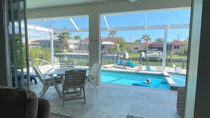 Ein verglaster Balkon mit Blick auf einen Swimmingpool, Liegestühle und einen Tisch.
