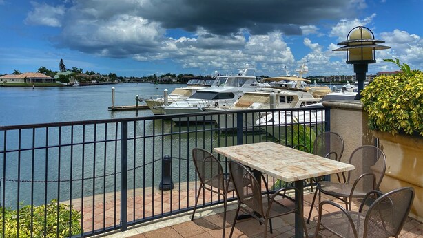 Eine Terrassenausrichtung am Wasser mit Tisch und Stühlen, mit Blick auf einen Yachthafen und Boote.