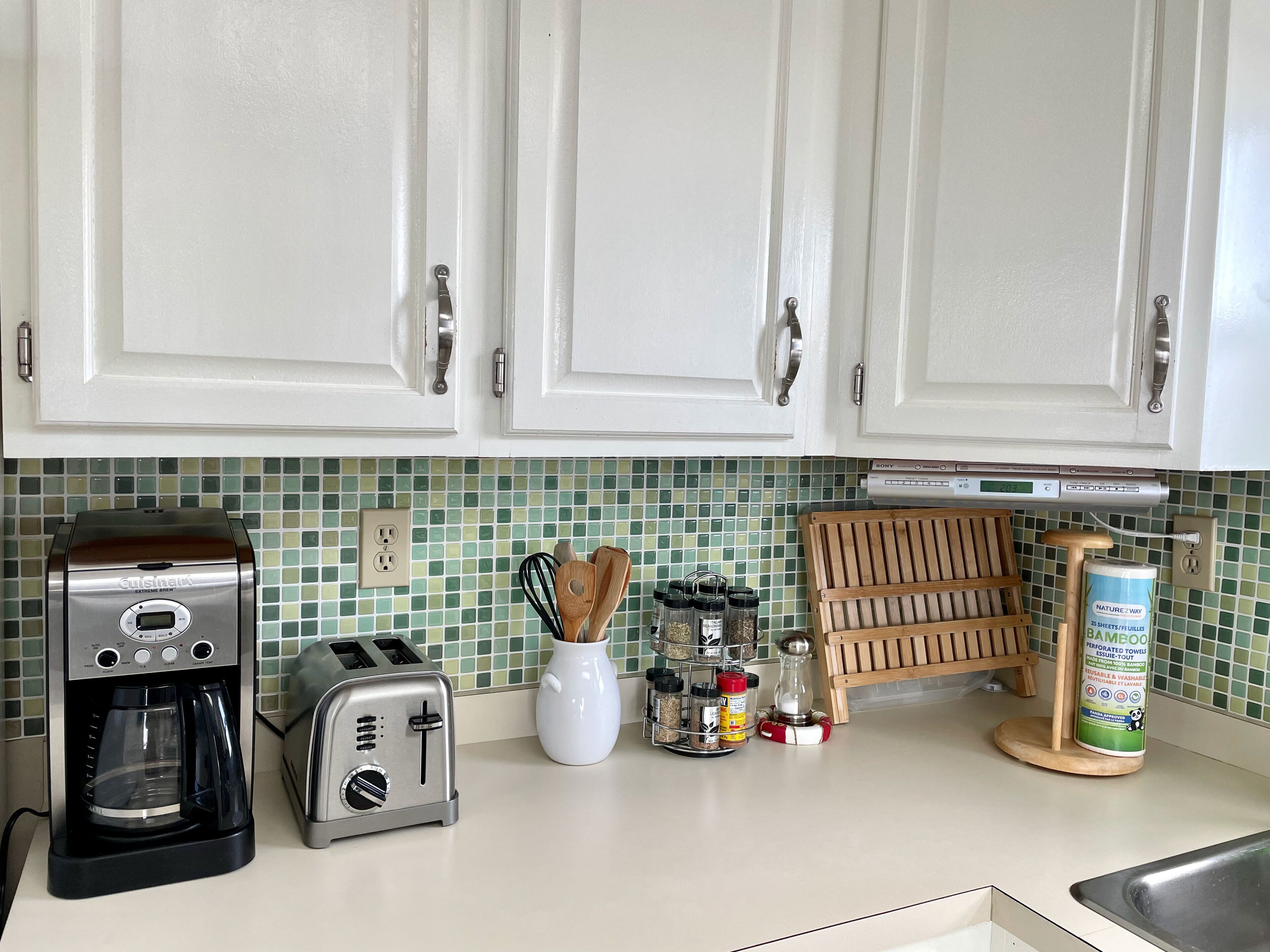 A kitchen with white cabinets, a coffee maker, a toaster, a spice rack, and a bamboo towel dispenser.