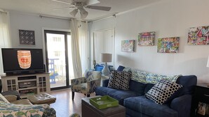 A living room with a blue sofa, patterned armchair, and ottoman. A television is on a cabinet, and there are paintings on the wall. - Flop On In: Bring your flipflops and enjoy the best of Myrtle Beach (Myrtle Beach)