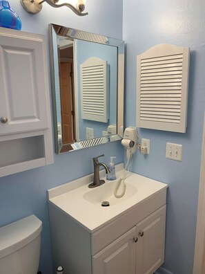 A bathroom with a white sink, a mirror, a hairdryer, and a towel dispenser.