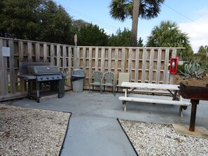 A backyard with a wooden fence, a grill, a trash can, a picnic table, and a bench.