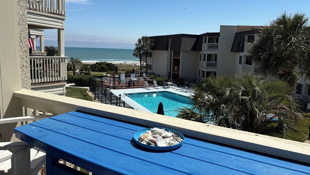 A pool area with a view of the ocean, a dining table with a plate of seashells, and a building with balconies. - Flop On In: Bring your flipflops and enjoy the best of Myrtle Beach (Myrtle Beach)