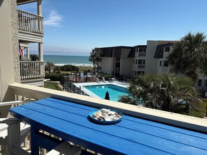 Une piscine avec vue sur l’océan, une table à manger ornée d’une assiette de coquillages et un bâtiment doté de balcons.