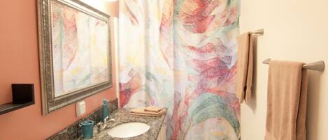 A bathroom with a granite countertop, a sink, a mirror, a shower curtain with a colorful abstract pattern, and a towel rack with a towel.