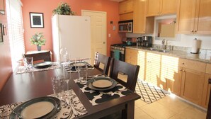 Un coin repas avec une table dressée pour quatre personnes, un réfrigérateur et des meubles en bois en arrière-plan.