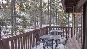 Eine Holzterrasse mit Metalltischen und -stühlen, umgeben von Bäumen.