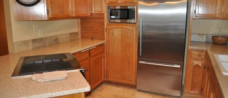 A kitchen with wooden cabinets, a stainless steel refrigerator, a microwave, and a clock on the wall.