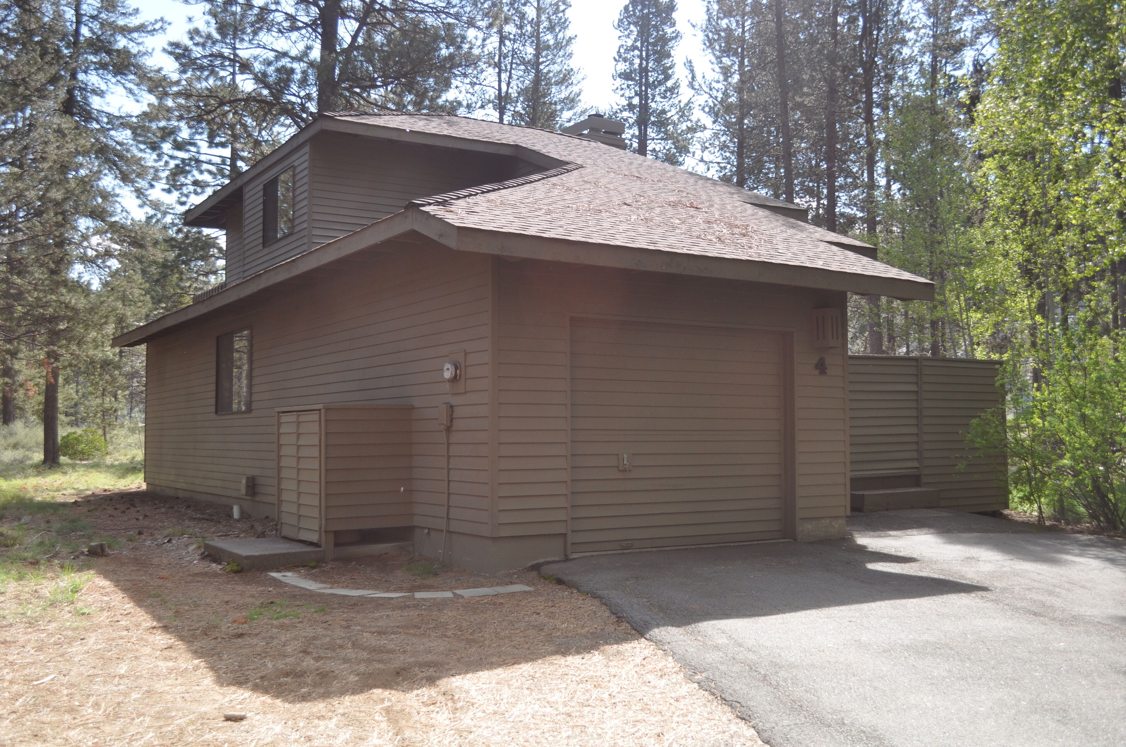 A two-story cabin with a sloped roof, a front garage door, and a driveway leading to the entrance.
