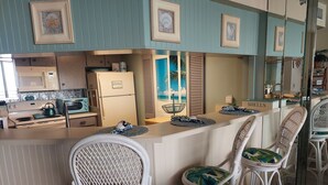 Eine Küche mit Kühlschrank, Mikrowelle, Herd und einem Essbereich mit Korbstühlen und einer Arbeitsplatte.