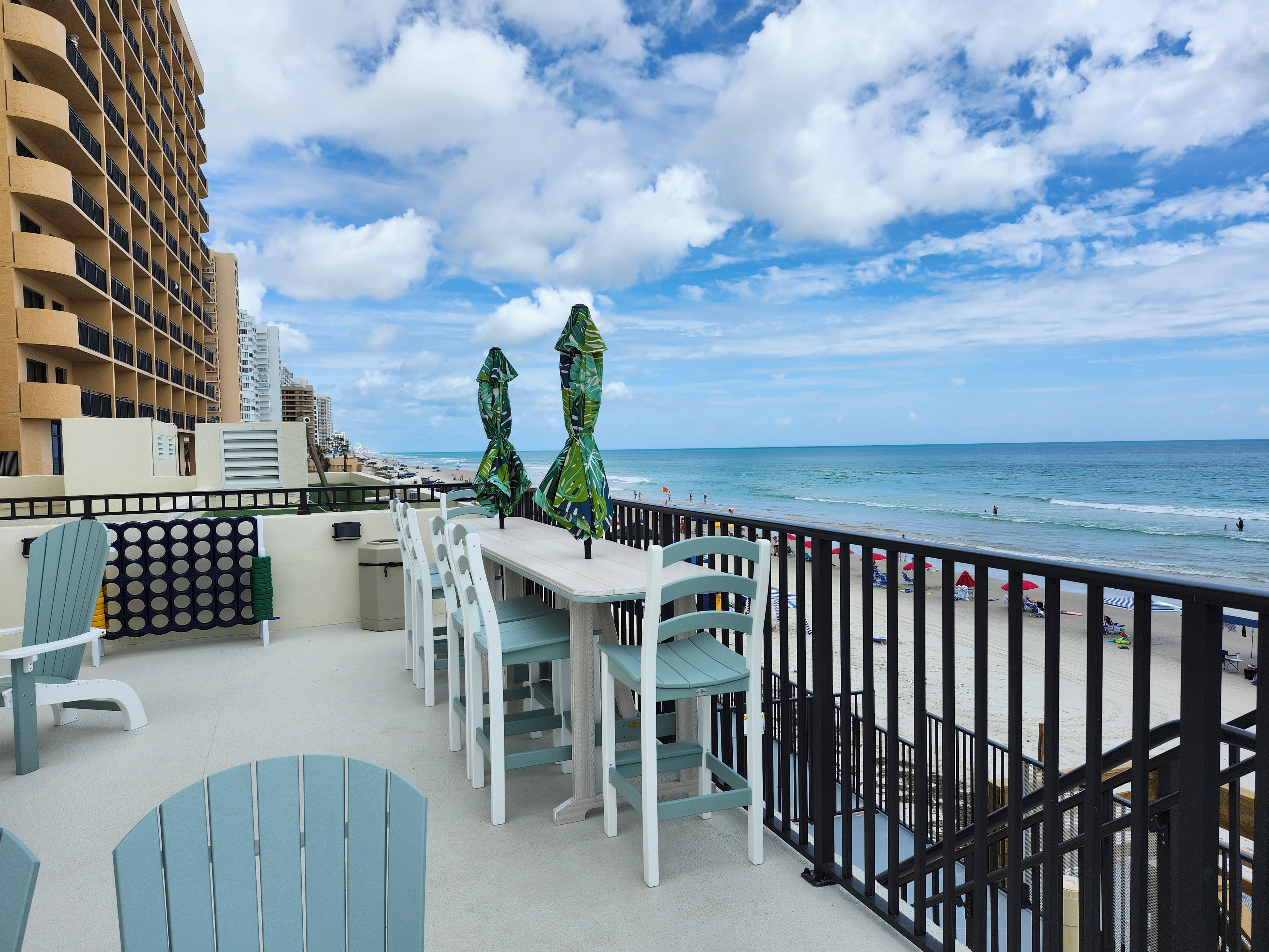 A balcony with outdoor seating, a view of the beach, and a tall building in the background.