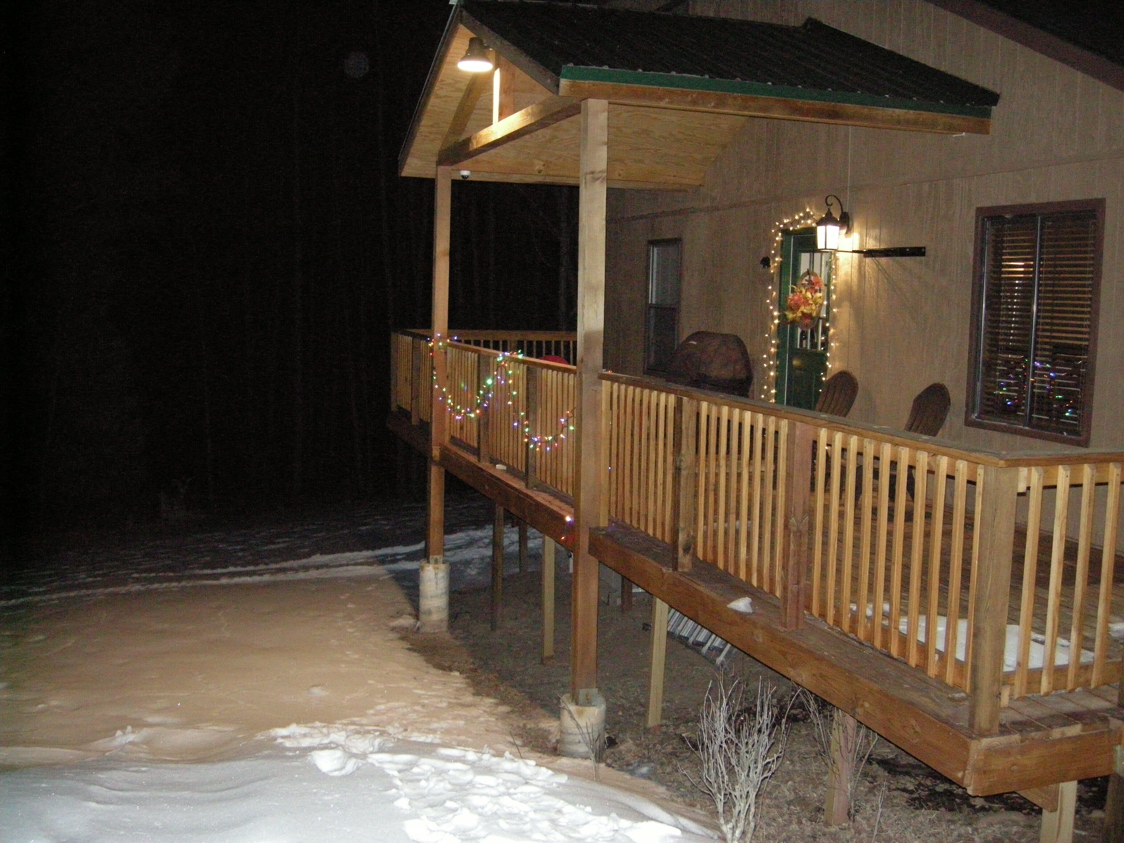 A wooden porch with railings, a covered area with a roof, and a window with blinds.