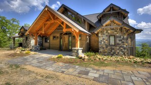 Une cabane en rondins avec une façade en pierre, une véranda en bois et une cheminée en pierre.