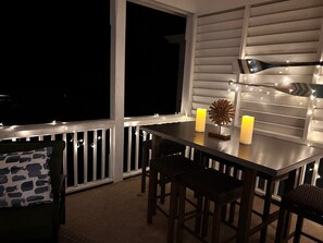 A balcony with a table, chairs, candles, and string lights.