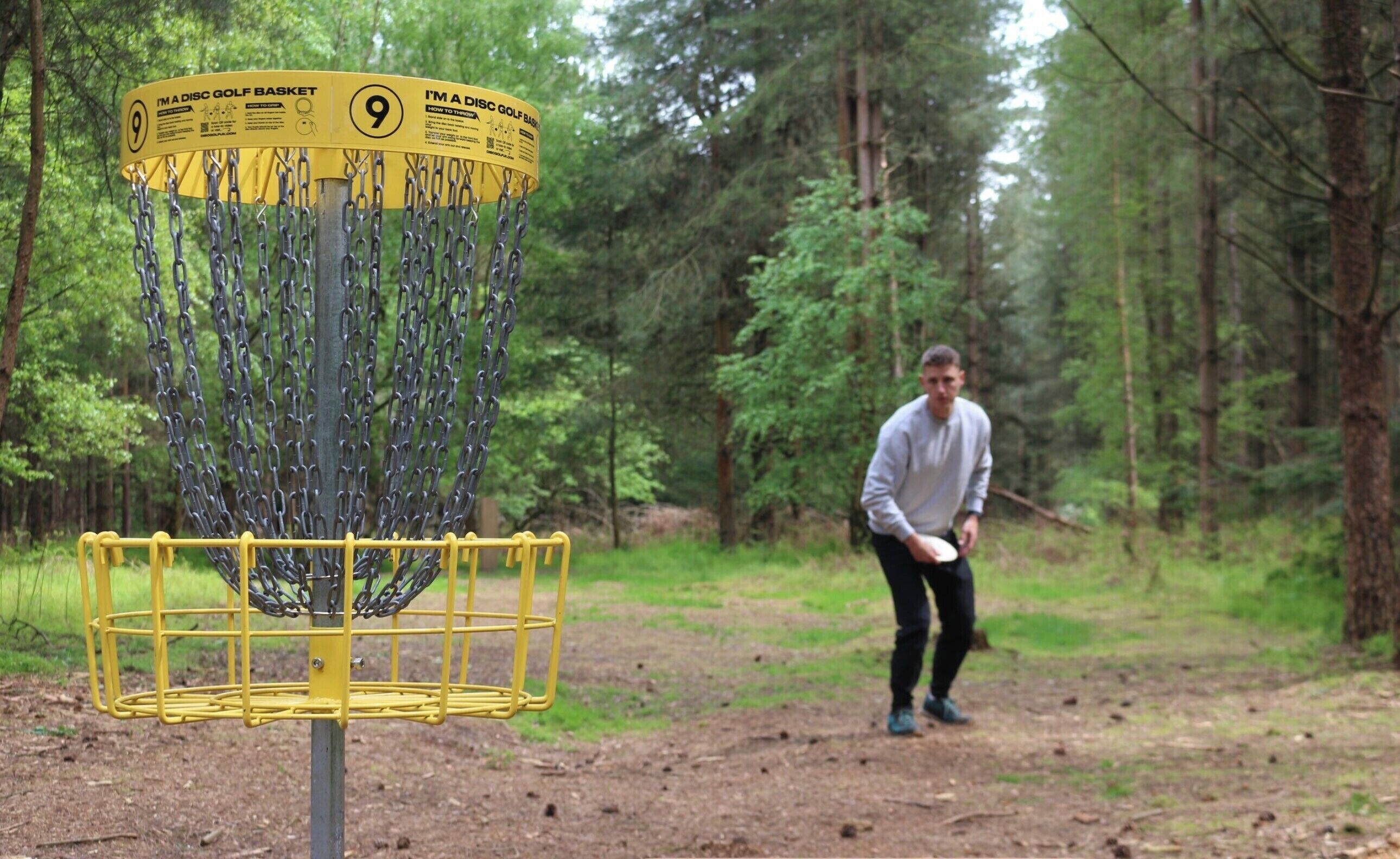 A disc golf basket with a chain barrier and a sign indicating it's a disc golf basket.