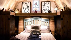 Un dormitorio acogedor en el ático con techo inclinado, cabecera de madera y cama con dos almohadas. Sobre la cama, hay dos letreros con el alfabeto.