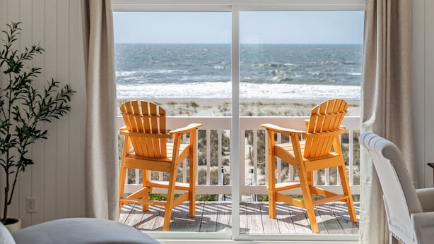 A balcony with two wooden chairs facing a view of the ocean. - Luxury Oceanfront Retreat: Concierge Beach Tent Service, Heated Pool & Hot Tub (Holden Beach)