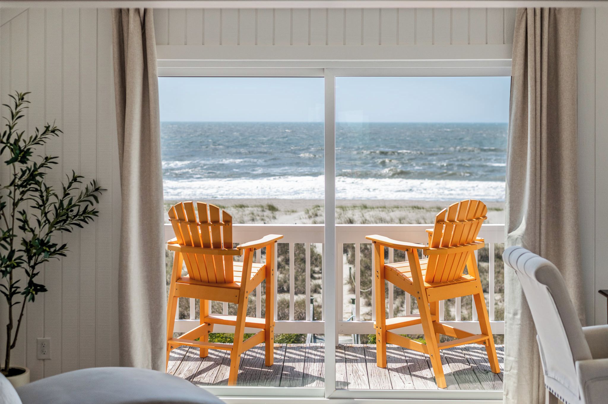 A balcony with two wooden chairs facing a view of the ocean.