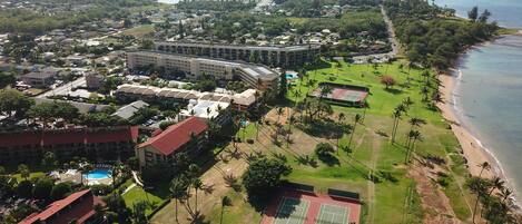 An aerial view of a coastal resort with multiple buildings, a beach, and tennis courts.