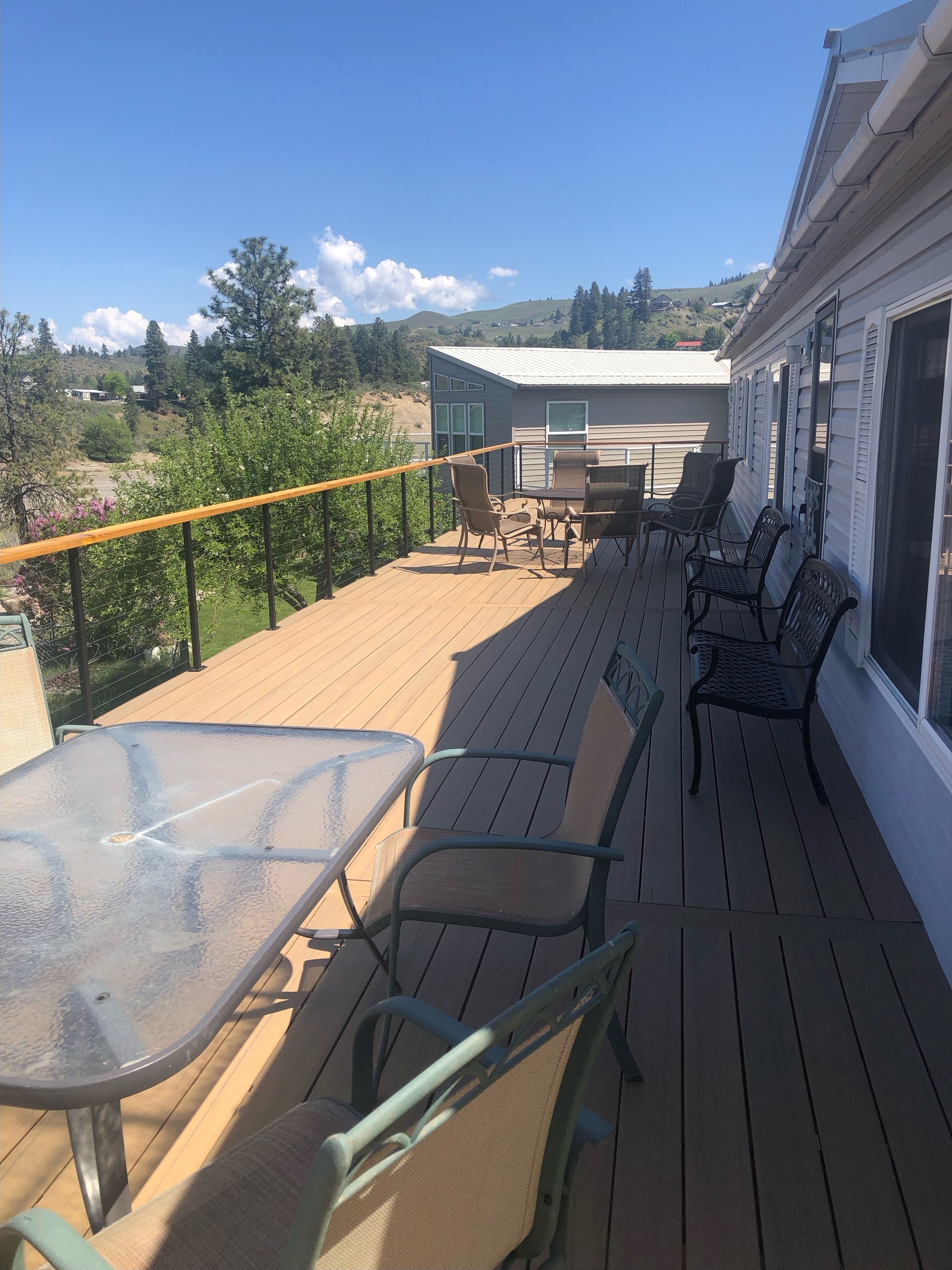 Una terraza de madera con mobiliario exterior, incluyendo una mesa y sillas, con vistas a un paisaje pintoresco con colinas y árboles.