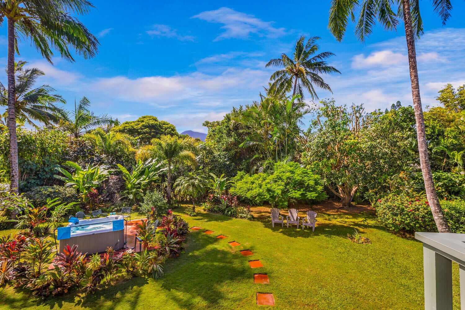 Un jardín exuberante con palmeras, un pequeño espacio de descanso con sillas y una estructura azul.