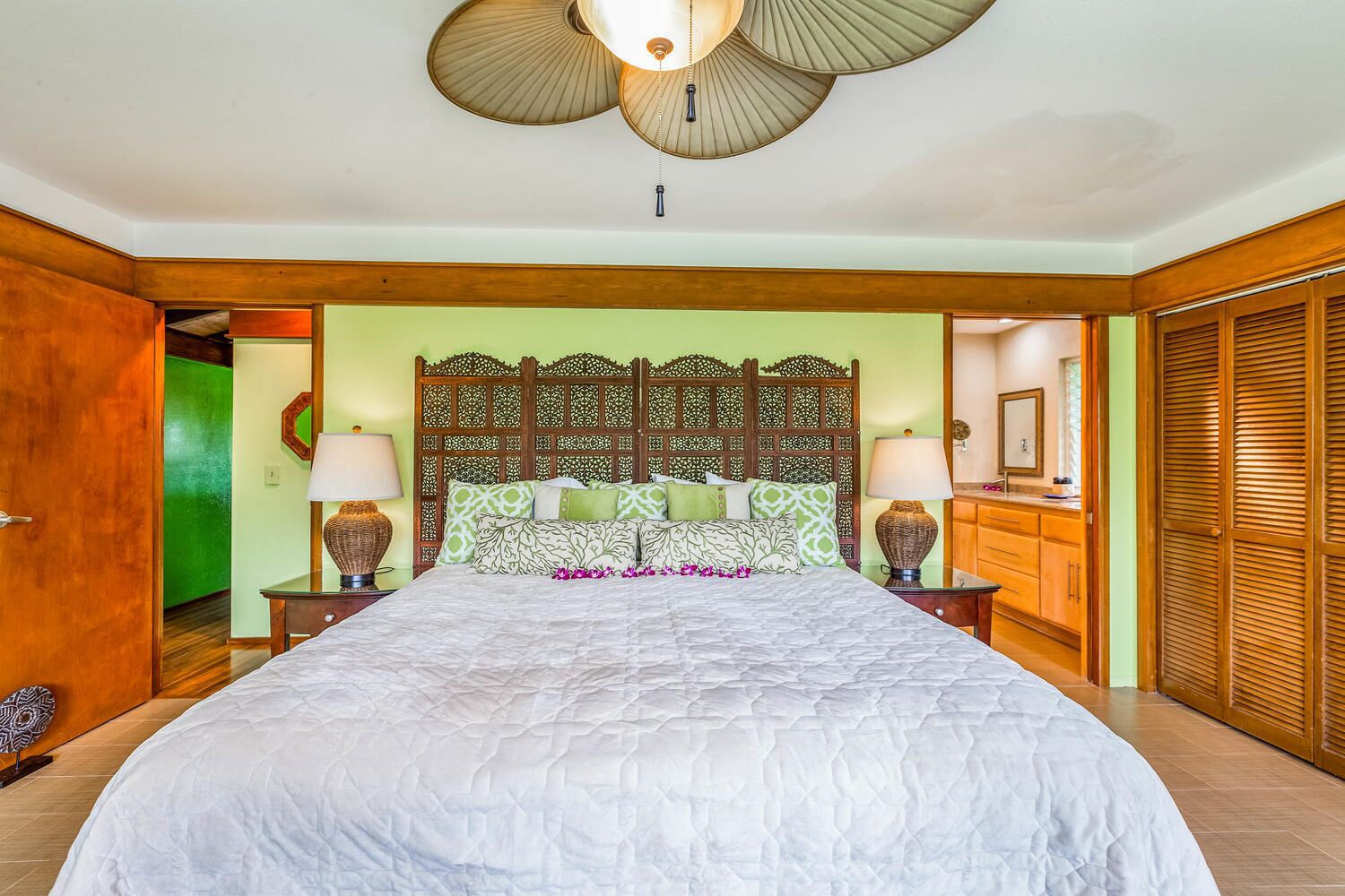 A bedroom with a large bed, wooden headboard, two bedside tables with lamps, a green wall, and a wooden wardrobe.