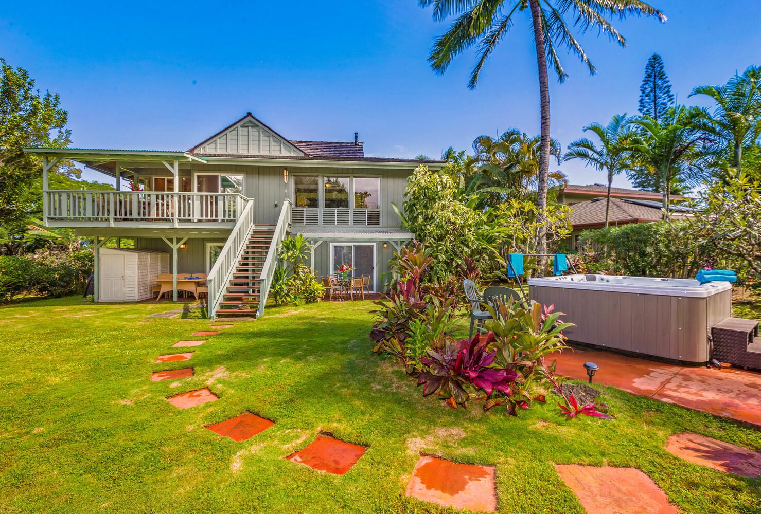 A two-story house with a covered porch, a hot tub, and a well-maintained garden with tropical plants.