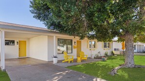 A modern house with a yellow door, large windows, and a covered porch with yellow Adirondack chairs. - Walk to Old Town, 3BR + Backyard (Scottsdale)