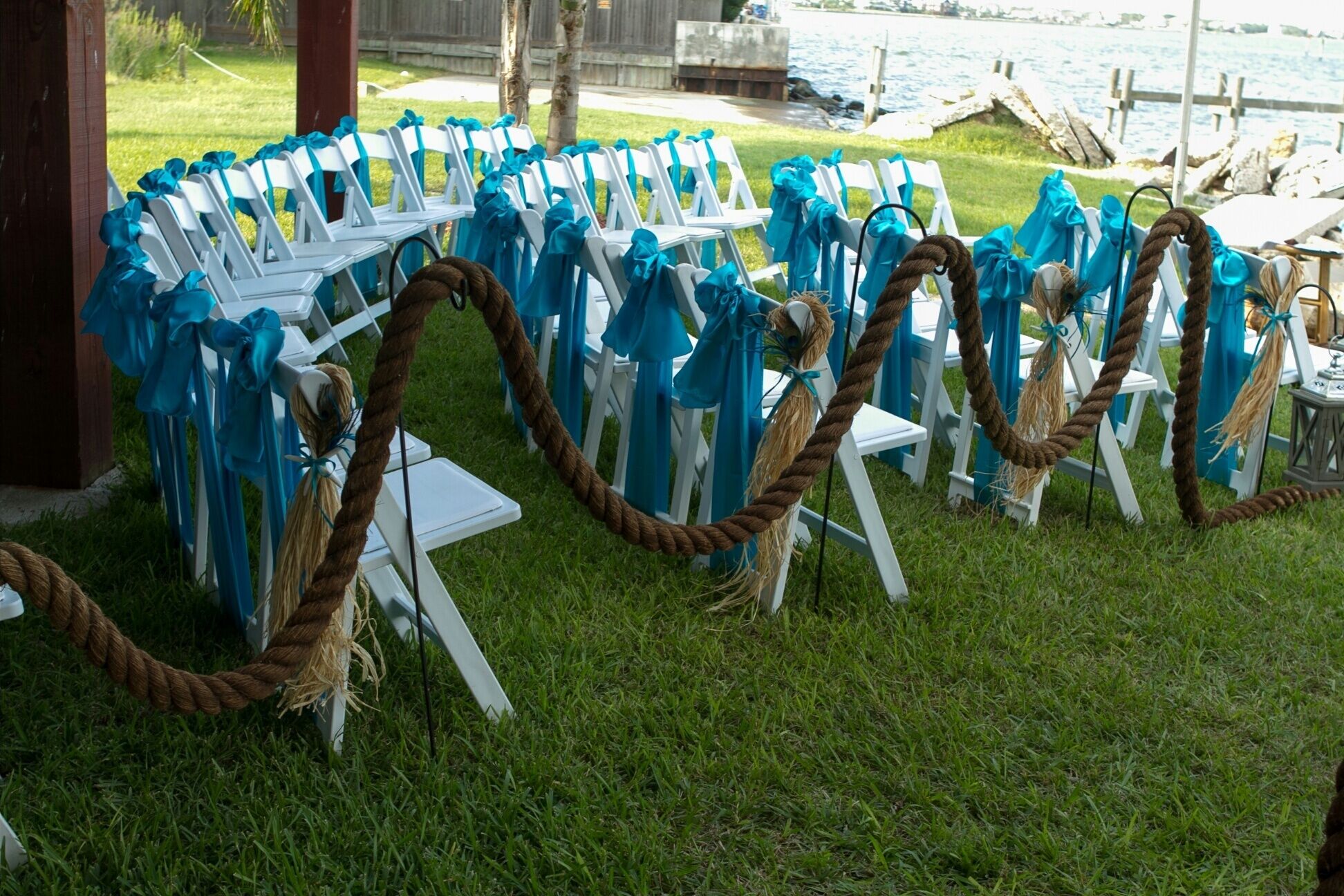 Outdoor seating with white chairs and blue accents, arranged on grass near a waterfront.