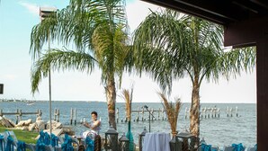 Eine Sitzgelegenheit im Freien an der Küste mit Stühlen und Tischen, Palmen und Blick auf das Meer.