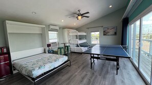 Ein Schlafzimmer mit Etagenbett, Schreibtisch, Stuhl, Bett mit Blumenmuster und Deckenventilator, sowie einem großen Fenster mit Blick auf Boote.