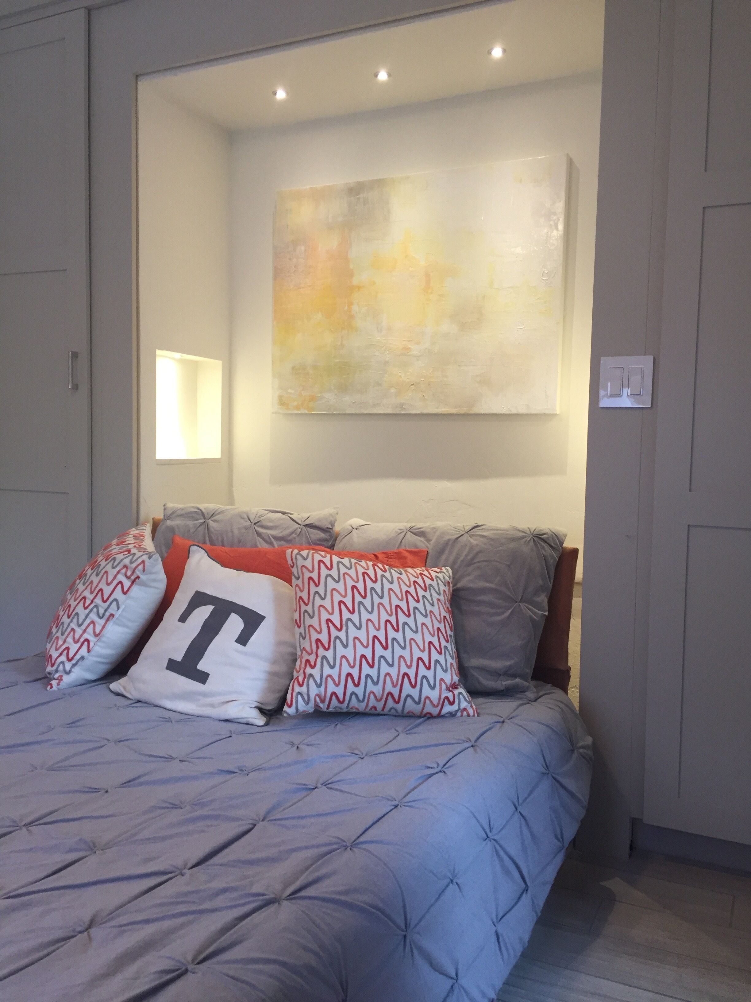 A bedroom with a bed, pillows, a wall-mounted abstract painting, and a window.