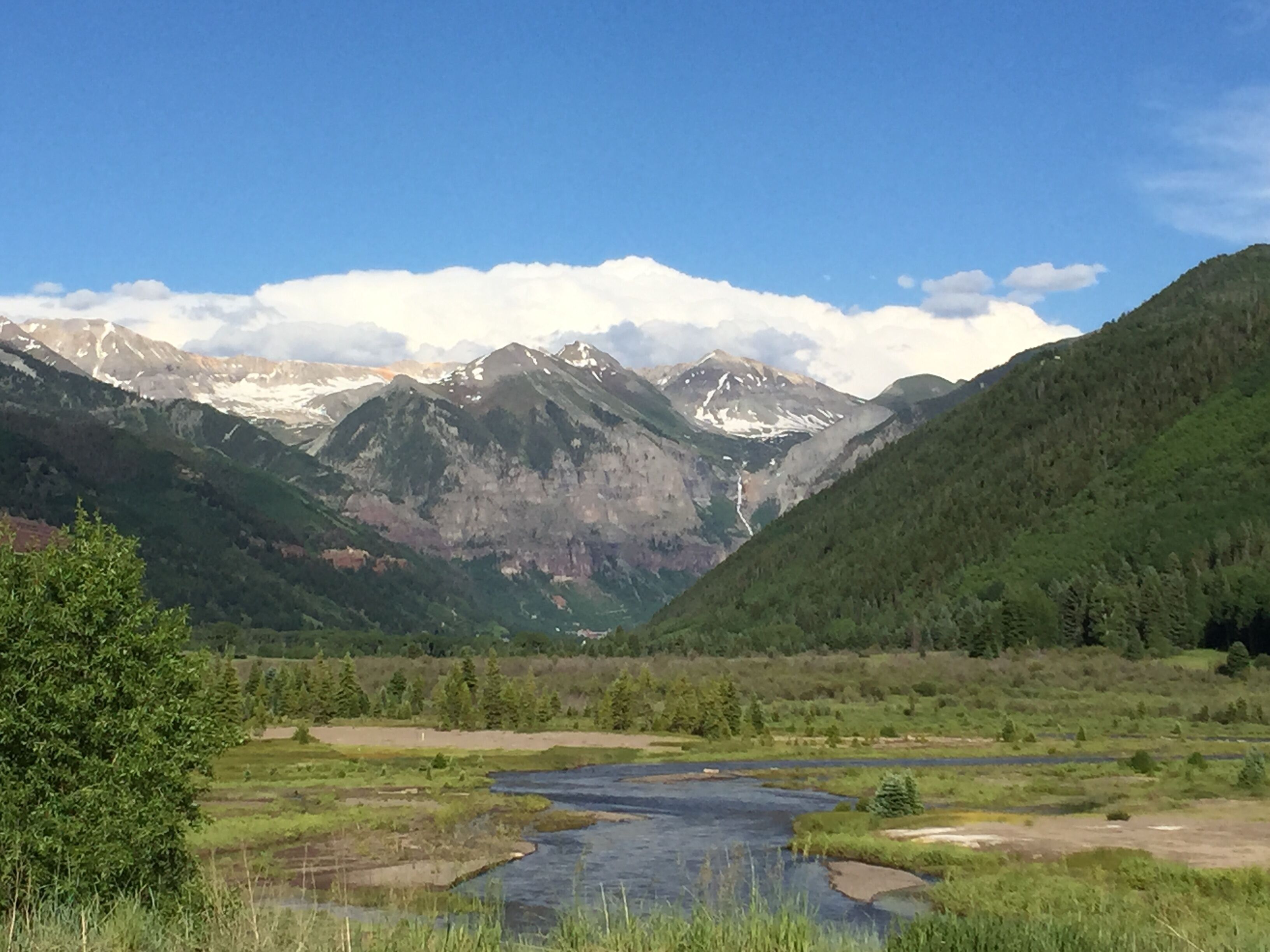Un paisaje montañoso con un río, un bosque denso y picos nevados.