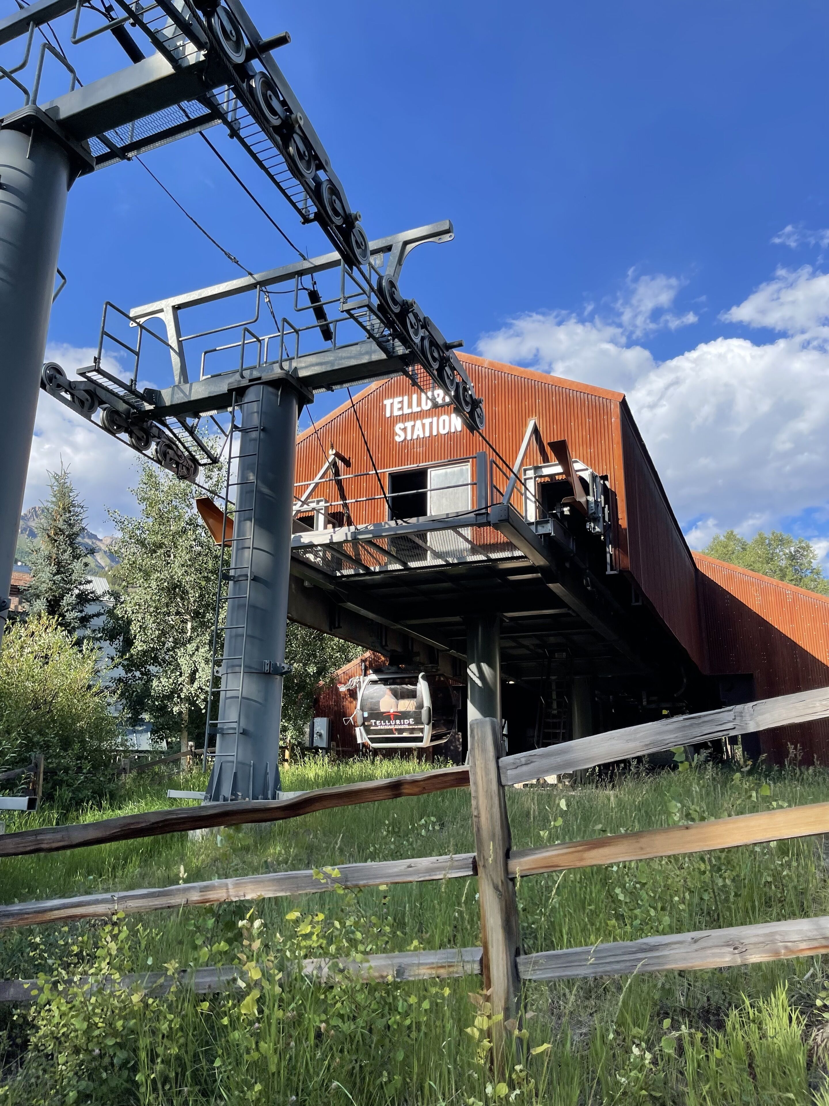 Una estación de tren con un edificio rojo identificado con el letrero "TELLURIPE STATION" y un tren en las vías.