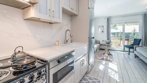 Une cuisine moderne équipée d’une cuisinière à gaz, d’un four et d’un réfrigérateur en acier inoxydable. On y trouve un coin repas avec une table et des chaises, ainsi qu’une vue sur l’extérieur grâce à de grandes fenêtres.