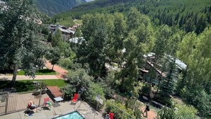 Un espace piscine comprenant deux piscines, entouré d’une clôture, d’arbres et offrant une vue sur les montagnes.