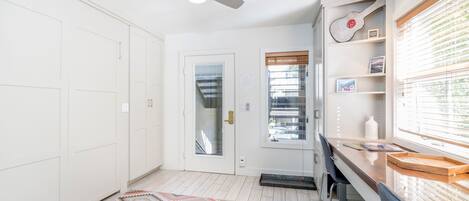 A modern kitchen with a built-in oven, a microwave, and a sink. There is a window with blinds and a door leading to the outside.