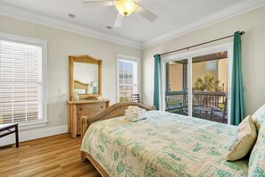 Une chambre avec un grand lit, un ventilateur de plafond, une commode et un balcon avec vue.