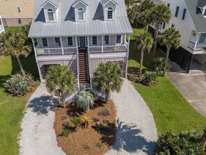 Une maison à deux étages dotée d’un balcon, entourée de palmiers et d’une pelouse bien entretenue.