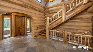 Ein rustikales Holzblockhaus-Interieur mit einer Holzwage, Steinfußboden und einer großen Holztür.