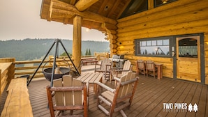 Eine Holzterrasse mit Sitzgelegenheiten, einem Grill und Blick auf eine malerische Berglandschaft.