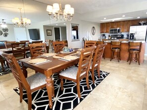 Un espace repas comprenant une table en bois, des chaises et un lustre. On y trouve également une cuisine avec des meubles et des appareils électroménagers en bois.