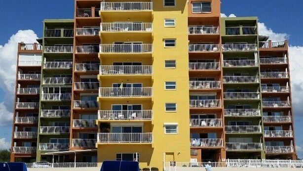 Un hôtel à plusieurs étages doté de balcons, situé en bord de plage, avec une étendue de sable fin devant et un ciel bleu dégagé.