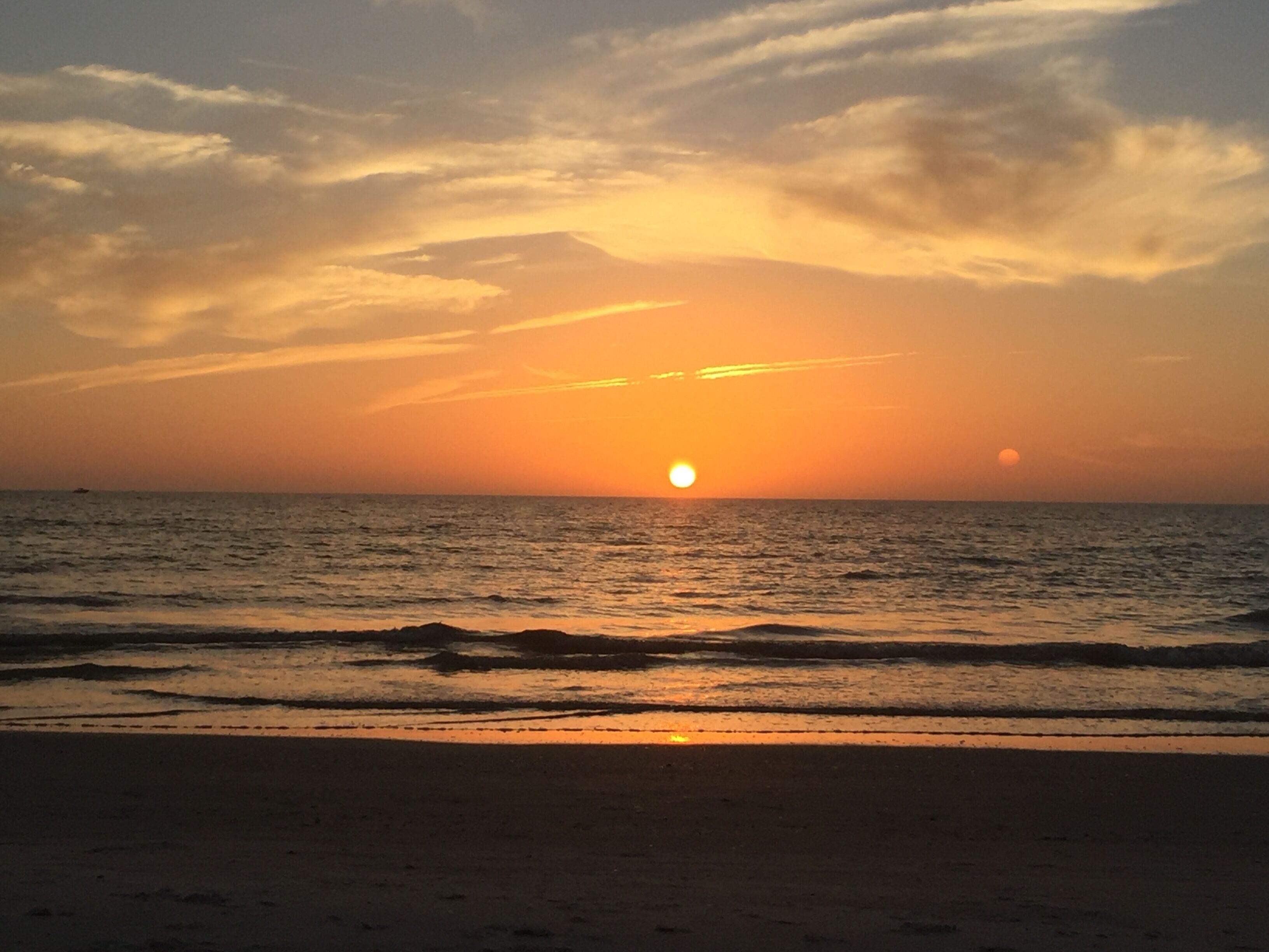 Tramonto su una spiaggia con onde calme e cielo sereno.