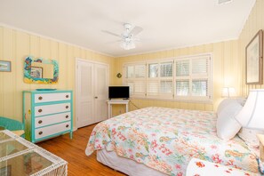 Un dormitorio con cama, cómoda, televisor y ventana con contraventanas.