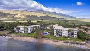 Un hôtel situé en bord de mer, avec plusieurs étages, une piscine et une vue sur le paysage environnant, notamment les montagnes et les palmiers.